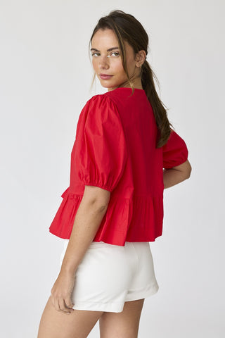 Back and side view of model wearing red puff sleeve cotton peplum top with gathered hem, paired with white shorts.