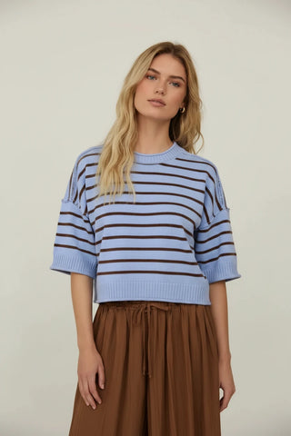 Woman wearing a blue and brown striped sweater and light blue skirt standing in front of a mirror.