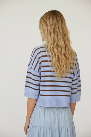 Woman wearing a striped sweater and skirt, looking at herself in a mirror.