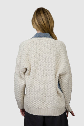 Person wearing a textured cream sweater with a wooden panel background