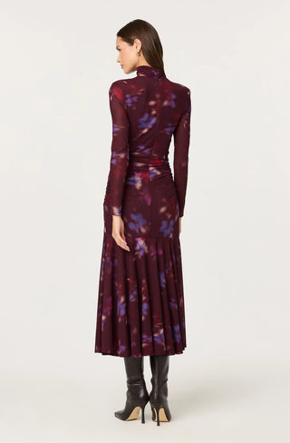 Woman wearing a long, dark purple dress with floral pattern on a white background