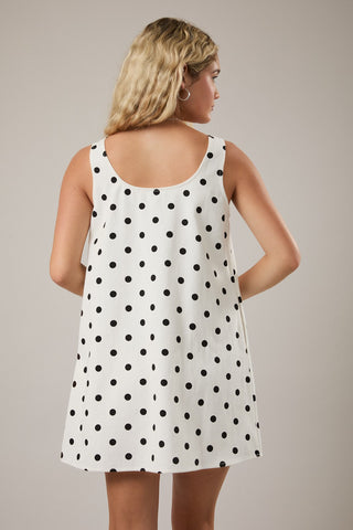 Woman wearing a white sleeveless dress with black polka dots against a neutral background