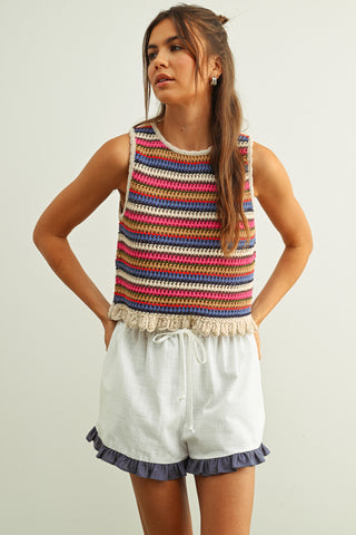 Woman wearing a colorful striped tank top and white shorts on a plain background