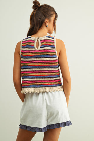 Woman wearing a colorful striped sleeveless top and white shorts on a plain background