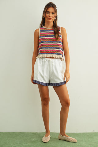 Woman wearing a colorful striped sleeveless top and white shorts on a plain background