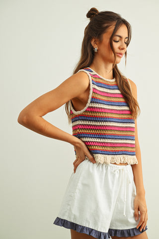 Woman wearing a colorful striped sleeveless top and white skirt against a plain background