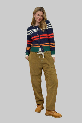 Woman wearing a colorful striped sweater and brown pants on a gray background
