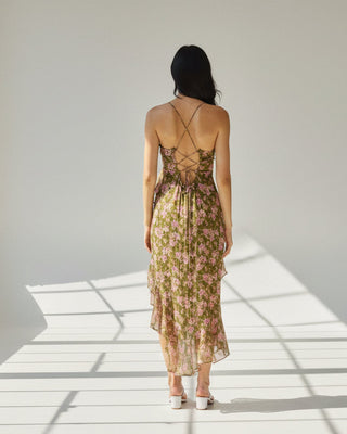 Woman in a floral dress standing outdoors with plants and a wall in the background