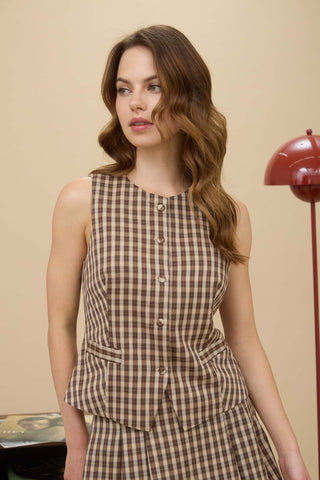 Woman wearing a brown checkered dress against a beige wall with a red lamp.