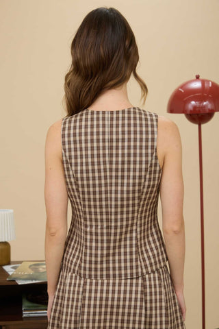 Woman wearing a brown checkered dress standing in a room with a red lamp and beige wall.
