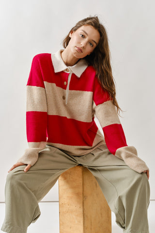 Woman wearing a red and beige striped sweater sitting on a wooden stool against a white background