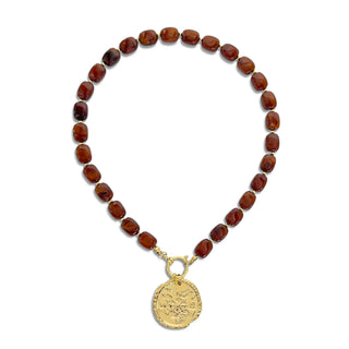A beaded necklace featuring polished reddish-brown gemstone beads and a gold-toned circular pendant with an embossed design, displayed on a clean white background.