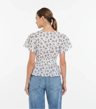 Woman wearing a floral blouse and blue jeans against a red background