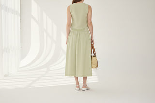 Woman wearing a light green dress holding a straw bag indoors.