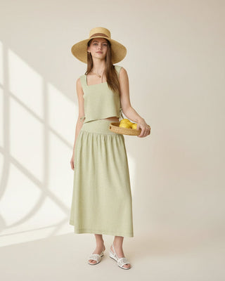 Woman in a light green dress and hat holding a basket of lemons in a room with decorative elements.
