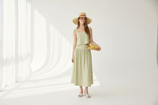 Woman in a light green dress and hat holding a basket of lemons in a room with decorative elements.