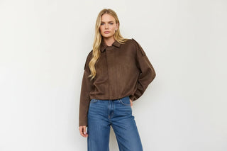 A blonde model wearing a brown cropped faux-suede jacket and a white cow-print mini skirt, posing against a plain white studio background.