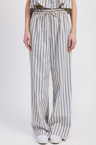 Close-up front view of a woman wearing high-waisted wide-leg pants with vertical blue stripes and a drawstring waist, paired with white sneakers against a plain studio background