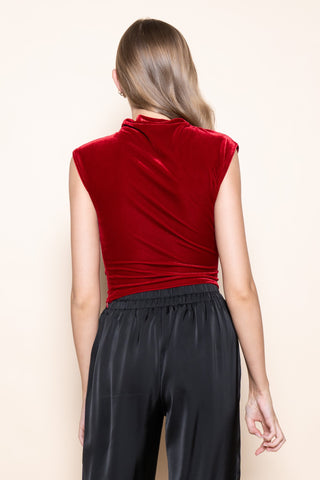 Woman wearing a red sleeveless top and black pants on a beige background