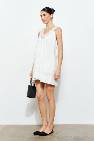 Woman wearing a white sleeveless dress with a black handbag on a white background