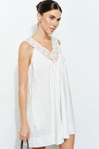 Woman wearing a white sleeveless dress with lace details on a plain background