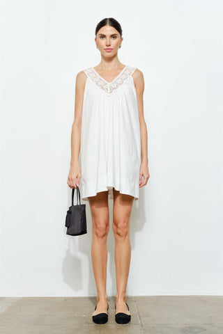 Woman wearing a white sleeveless dress with lace details on a plain background