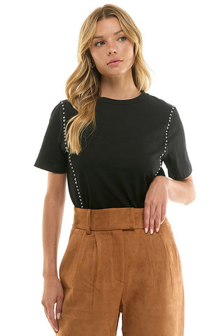 Woman wearing a black top with decorative straps and brown pants on a white background