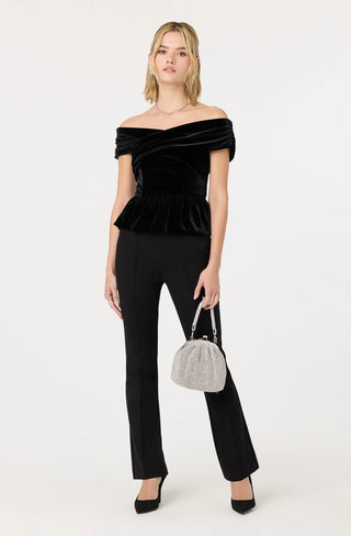Woman wearing a black off-shoulder top and black pants, holding a silver handbag on a white background