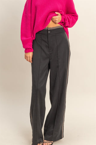 Person wearing a bright pink sweater and black pants on a beige background