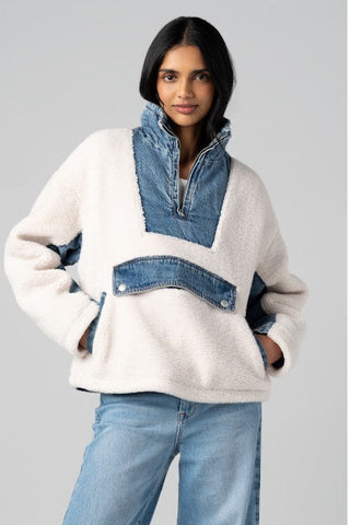 Woman wearing a white sweater with denim accents on a gray background
