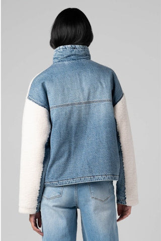 Person wearing a denim jacket with white sleeves on a gray background