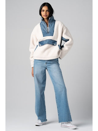 Woman wearing a white sweater with denim accents and blue jeans on a gray background