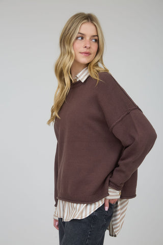 Woman wearing a brown sweater over a striped shirt on a plain background