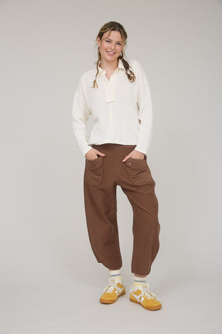 Woman wearing a white blouse and brown pants on a plain background