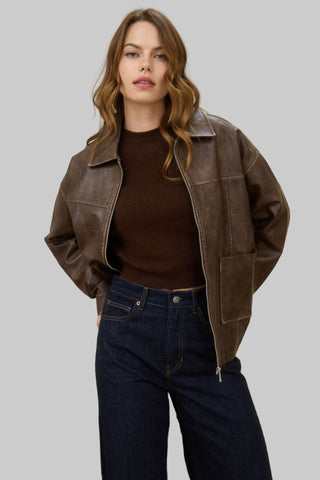 Woman wearing a brown leather jacket and dark jeans against a beige background