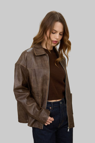 Woman wearing a brown leather jacket and dark jeans standing in a room with a red lamp.