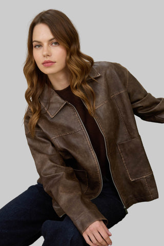 Woman wearing a brown leather jacket sitting on a green chair against a beige background