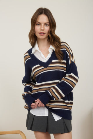 Woman wearing a striped sweater over a white shirt and black pleated skirt on a plain background