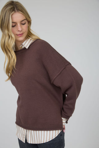 Woman wearing a brown sweater over a striped shirt on a plain background