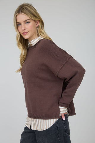 Woman wearing a brown sweater over a striped shirt on a plain background