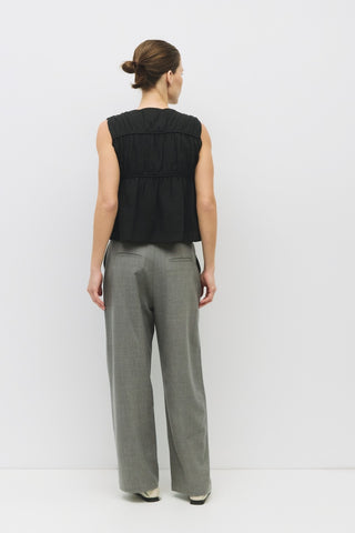 Back view of sleeveless black cotton top with ruched paneling and cropped fit, paired with gray wide-leg trousers