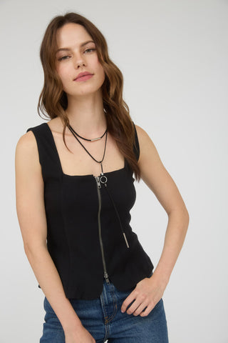 Woman wearing a black sleeveless top with a zipper and blue jeans on a white background
