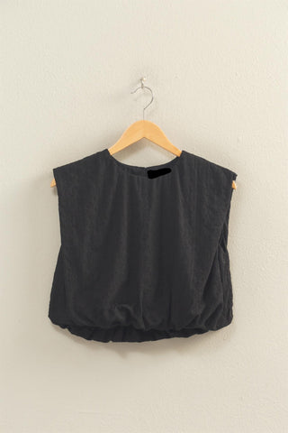 Black sleeveless top on a wooden hanger against a beige wall