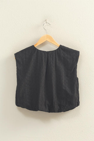 Black sleeveless top on a wooden hanger against a beige background