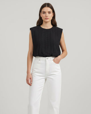 Black sleeveless top on a wooden hanger against a beige wall
