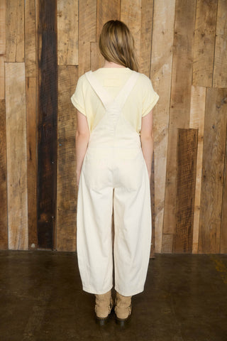 Person wearing a light-colored outfit standing against a wooden paneled wall.