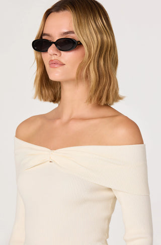 Woman wearing a cream off-shoulder top and black sunglasses against a white background
