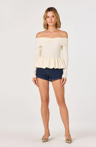 Woman wearing a white off-shoulder top and denim shorts on a white background