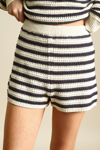 Person wearing a striped sweater and shorts on a beige background