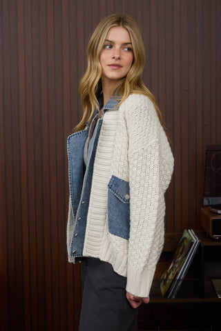 Woman wearing a white knitted cardigan over a denim jacket indoors.